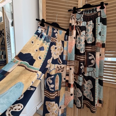 Calças compridas largas com padrão abstrato colorido penduradas em cabides pretos