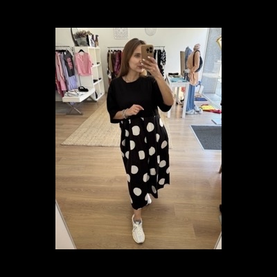 Mulher vestindo vestido preto com bolinhas brancas e ténis brancos numa loja de roupas