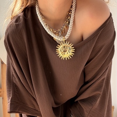 Mulher com colar de sol dourado, colar de contas castanhas, brincos argola dourados e camisola castanha solta.
