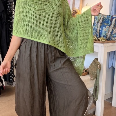 Mulher com capa verde de malha e calças largas castanhas no interior