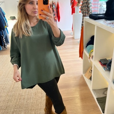 Mulher a tirar selfie com túnica verde, leggings pretas e botas castanhas numa loja de roupa