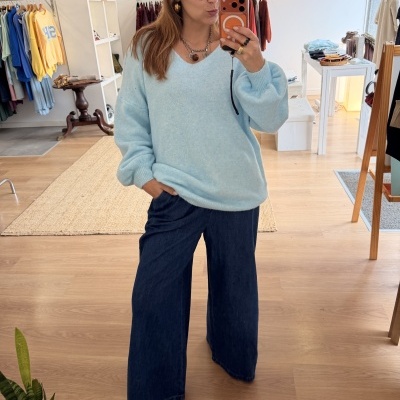 Pessoa vestindo camisola de malha azul clara e calças largas de ganga a tirar selfie numa loja de roupa