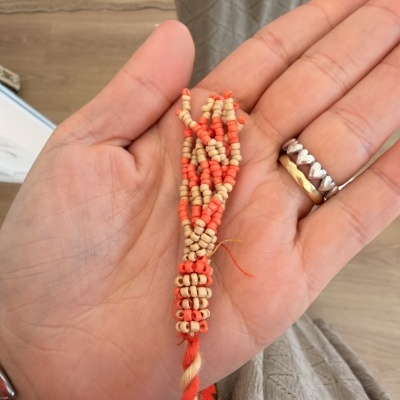 Pulseira de contas laranja e beje na mão com anéis