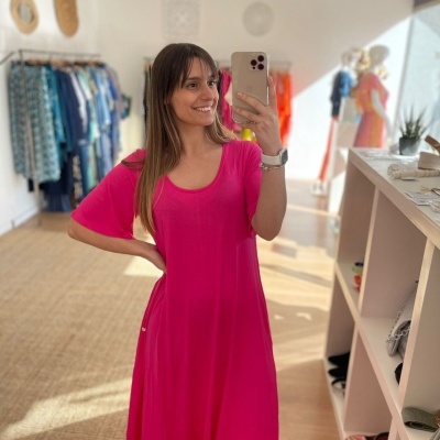 Mulher a usar um vestido rosa vibrante com manga curta, a tirar selfie numa loja de roupas