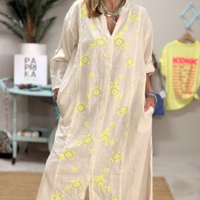 Vestido bege bordado com flores amarelas e botões frontais, usado com sandálias castanhas com detalhes dourados