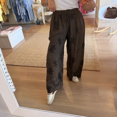 Calças largas castanhas com padrão floral bordado preto numa loja de roupas