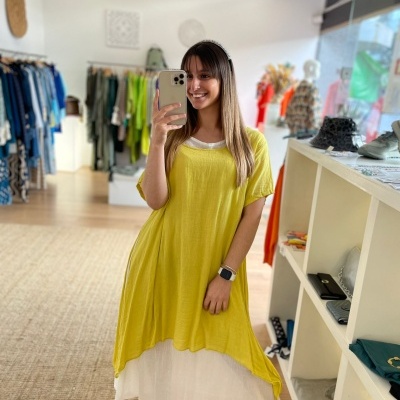 Mulher com vestido amarelo de malha e vestido branco por baixo em loja de roupas