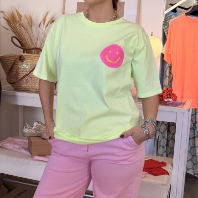 Mulher com camisola verde claro e padrão sorridente cor-de-rosa e calças largas lilás em espaço interior com acessórios e roupas