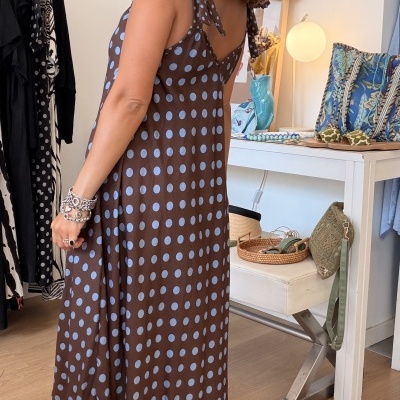 Mulher de costas vestindo vestido castanho com bolas azuis e laços nos ombros