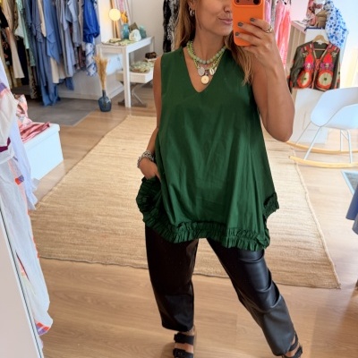 Mulher em loja a tirar selfie usando top verde com barra folhada e calças pretas.