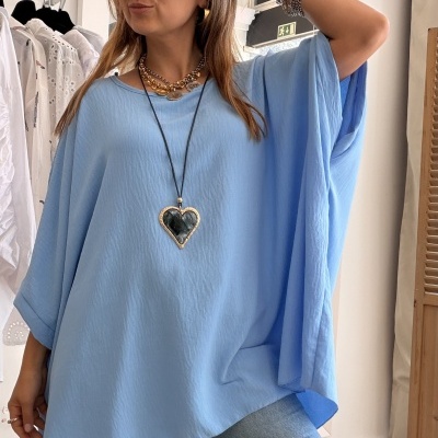 Mulher com blusa azul clara e colar de coração preto em interior