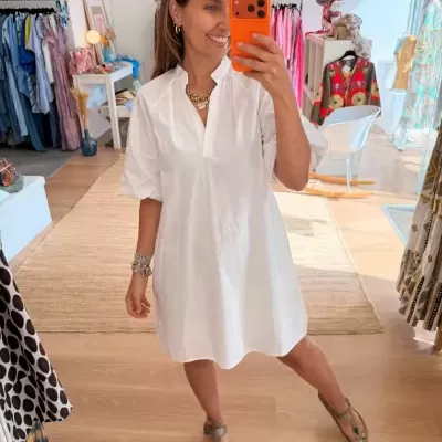 Vestido branco de manga curta com gola alta num cenário de loja de roupa.