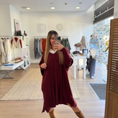 Mulher a tirar selfie com vestido bordô e botas castanhas numa loja de roupas moderna