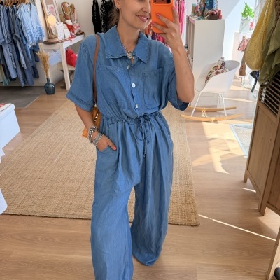 Mulher a vestir macacão azul claro com gola e bolsos, a tirar selfie num espelho em loja de roupa.