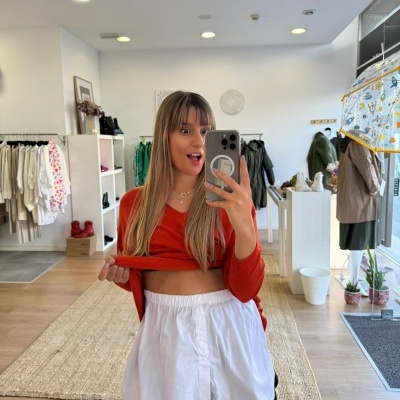 Pessoa num top vermelho e calções brancos numa loja de roupa com paredes brancas e chão de madeira.