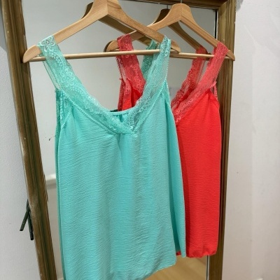 Dois tops de alças em renda azul-turquesa e vermelho pendurados em cabides de madeira num espelho com moldura castanha.