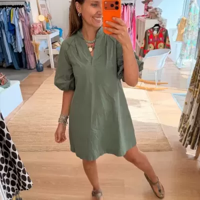 Mulher tira selfie usando vestido verde com mangas bufantes em loja de roupas