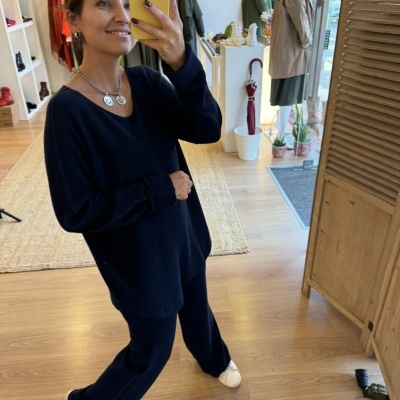 Mulher com conjunto preto de malha a tirar selfie em espelho numa loja com decoração de madeira