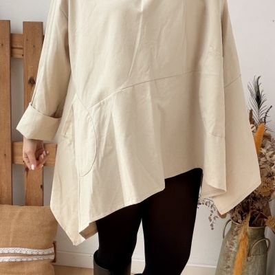 Mulher com blusa bege oversize, leggings pretas e botas pretas em ambiente interior com almofada bege e jarro com plantas secas