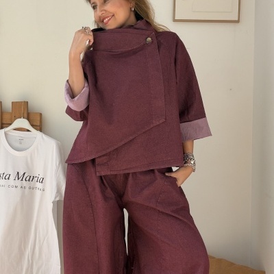 Conjunto vinho de casaco e calças largas com detalhes em mauve, mulher a segurar a gola do casaco.