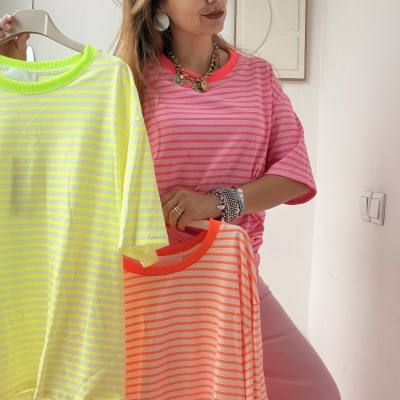 Mulher segura t-shirts às riscas amarelas e laranjas, vestindo t-shirt rosa às riscas
