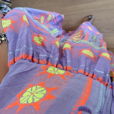 Vestido ou saia lilás com bordados em néon laranja e verde, vista de cima sobre chão de madeira