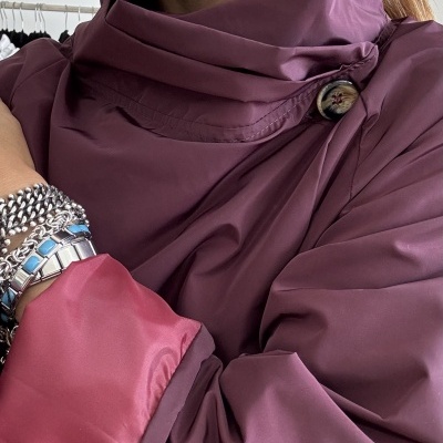 Casaco vinho com botão e gola alta usado por mulher com brincos e pulseiras.