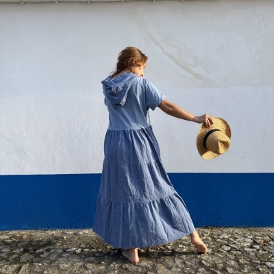 Pessoa de costas com vestido azul e chapéu de palha em parede branca e azul
