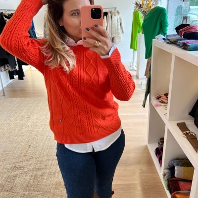 Mulher com suéter laranja trançado a tirar selfie numa loja de roupas