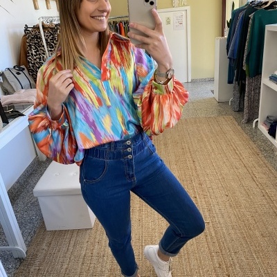 Mulher com camisa colorida e calças de ganga azuis a tirar selfie numa loja