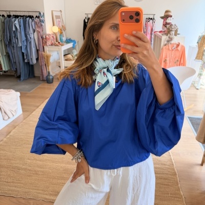 Pessoa com blusa azul de manga larga e calças brancas em loja de roupa.