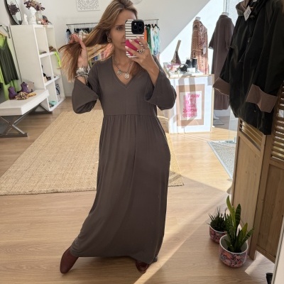 Mulher a usar vestido longo castanho com decote em V e mangas 3/4 numa loja de roupas