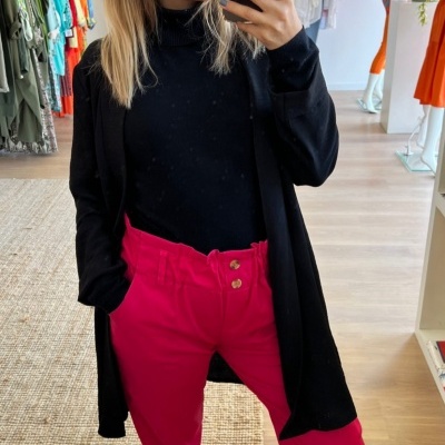 Mulher a usar calças anabela rosa com blusa e casaco pretos e sapatos pretos num espaço comercial