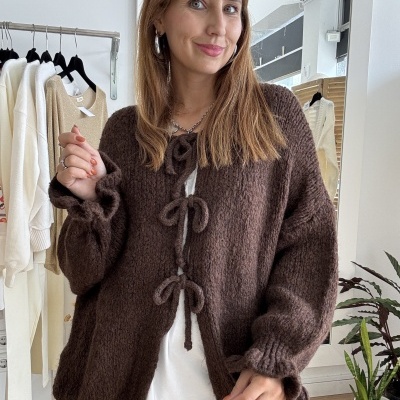 Mulher a usar casaco de malha castanho escuro com laços, calças com bolinhas brancas e camisola branca