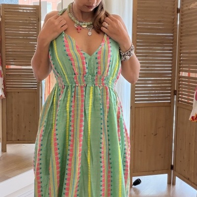 Vestido verde com listras coloridas usado por mulher numa loja com divisórias de madeira