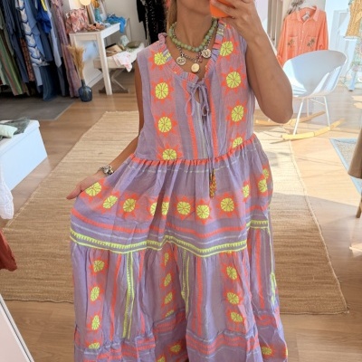 Vestido lilás com flores amarelas e detalhes laranja mostrado numa selfie de corpo inteiro em loja de roupa.