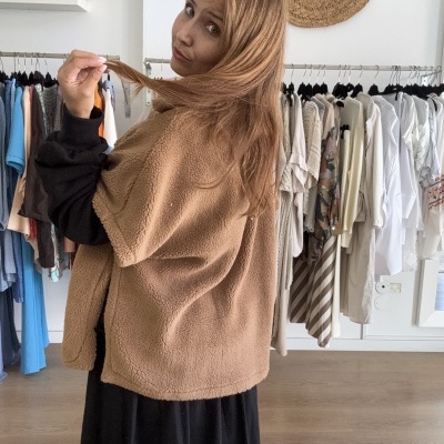 Mulher a usar casaco bege de tecido peludo em loja de roupa com roupas penduradas ao fundo