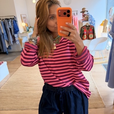 Blusa às riscas rosa e roxa com calças azul-escuras em selfie numa loja de roupa
