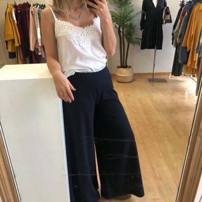 Mulher de blusa branca e calças largas pretas a tirar selfie em loja de roupa