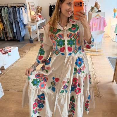 Vestido comprido creme com bordados coloridos usado por mulher a tirar selfie numa loja