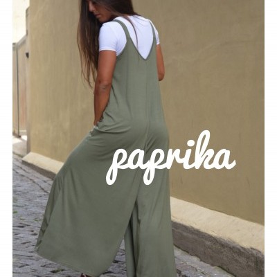 Mulher de costas usando macacão verde-oliva com t-shirt branca, em rua de pedra