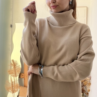 Mulher com camisola bege de gola alta e pulseiras no pulso