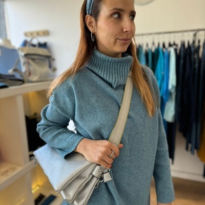 Mulher com suéter azul, faixa de cabelo e bolsa cinza em loja