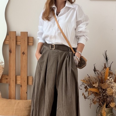 Mulher de camisa branca e saia plissada castanha com bolsa castanha e acessórios em ambiente decorado