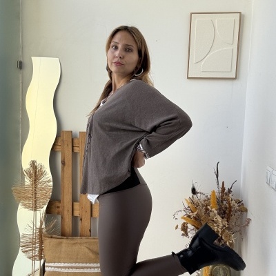 Mulher com leggings castanhas, camisola castanha e botas pretas em ambiente interior com decoração