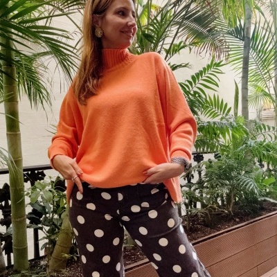 Pessoa com camisola laranja e calças de bolinhas junto a plantas