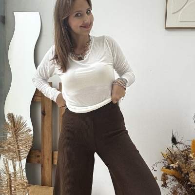 Mulher com camisola branca e calças largas castanhas numa sala com decoração rústica