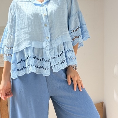Blusa azul clara com bordado e calças largas azuis em ambiente interior