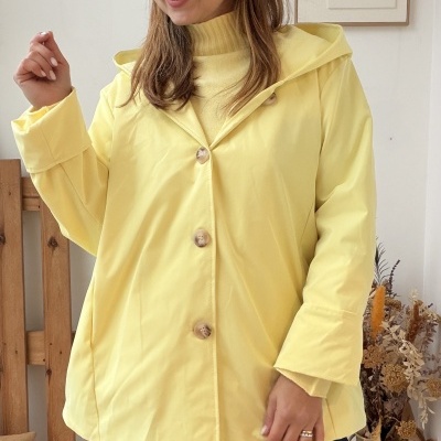 Mulher vestindo casaco amarelo com capuz e botões, camisola amarela e calças de ganga azul com decoração interior.