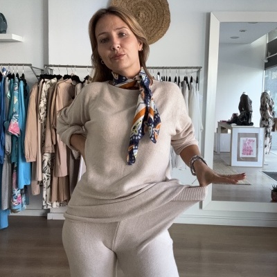 Mulher de roupa bege com cachecol colorido numa loja de roupa com cabides ao fundo.